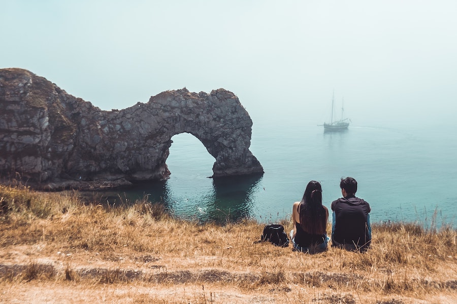 Couple sat overlooking sea with boat in the background.